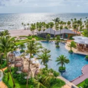 Vietnam tour package highlighting luxury beachfront resort with infinity pool, palm trees, tropical gardens, and stunning ocean view.